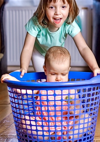 Mädchen schiebt Geschwister Baby im Wäschekorb 