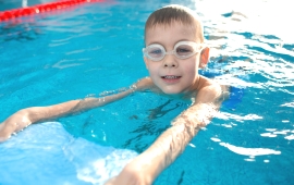 Junge mit Schwimmbrille und Schwimmbrett im Wasser 
