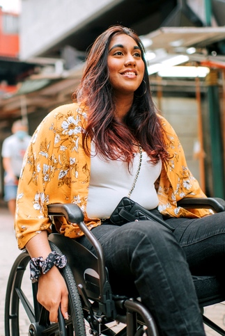Dunkelhäutige Frau mit langen Haaren lächelnd im Rollstuhl unterwegs