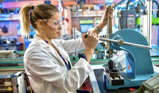 Frau mit Schutzbrille arbeitet mit Maschinen an einem technischen Arbeitsplatz 