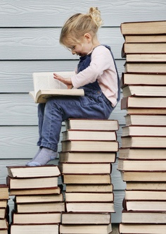 Kind sitzt auf einem Stapel Bücher und liest