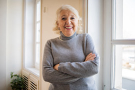 &Auml;ltere Dame mit verschr&auml;nkten Armen l&auml;chelnd in ihrer Wohnung 