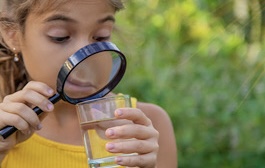 M&auml;dchen schaut mit einer Lupe in ein Glas Wasser 