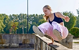 M&auml;dchen in rosa Jogginghose macht Parkours auf einer Mauer