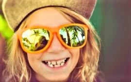 Mädchen mit Sonnebrille und Schildkappe lächelt ind Bild