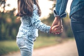 R&uuml;ckansicht Mutter und h&uuml;pfende Tochter an an der Hand, die einen Weg laufen 