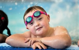 Lächelnder Junge mit Downsyndrom und Schwimmbrille am Beckenrand