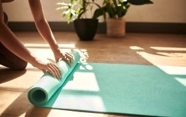 Frauenh&auml;nde rollen eine Yogamatte aus im Hintergund Sonnenlich und zweiZimmerpflanzen
