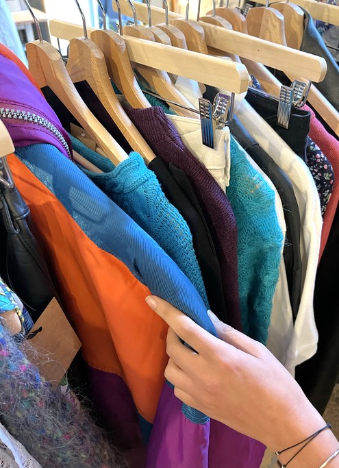 Frauenhand greift nach einem Kleidungsst&uuml;ck, das auf einer Kleiderstange h&auml;ngt