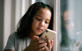 Mädchen vor dem Fenster mit Handy vor dem Gesicht