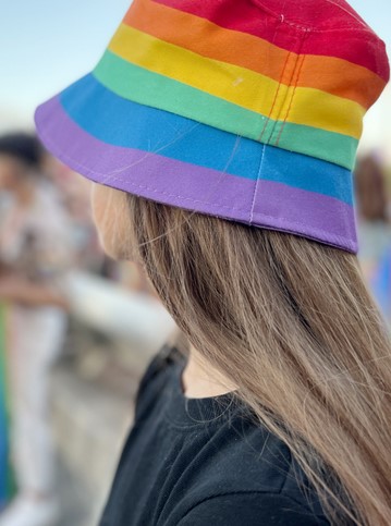 Mädchenkopf mit langen Haaren und Hut in Regenbogenfarben