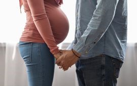 Mann und schwangere Frau stehen sich gegenüber und fassen sich an den Händen