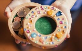 Kinderh&auml;nde halten eine runde Geldschatulle mit Glitzerperlen