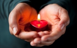 Zwei H&auml;nde halten ein rotes Herz mit brennender Kerze