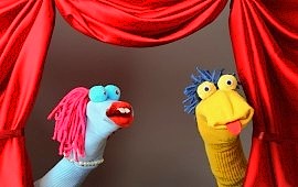 Zwei bunte Sockenpuppen auf einer B&uuml;hne mit rotem Theatervorhang