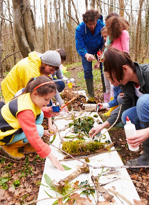 Kinder mit Betreuern auf einer Waldlichtung arbeiten mit Materialen aus dem Wald