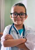 Mädchen mit großer Brille, weißem Kittel und Stethoskop spielt Ärztin
