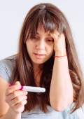 Frau schaut nachdenklich auf Schwangerschaftstest